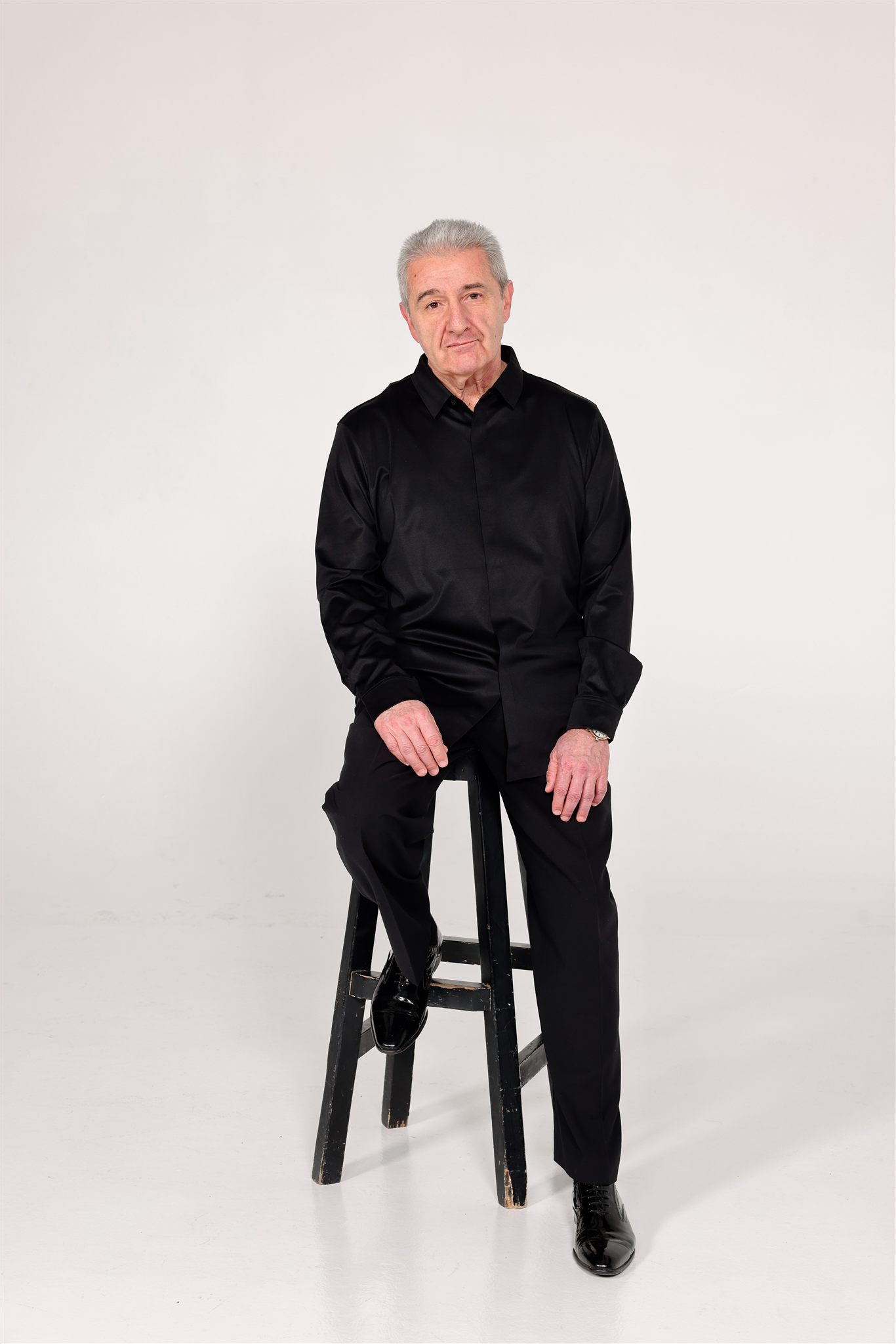 Studio portrait of conductor and pianist Vag Papian seated on a stool against a white studio background